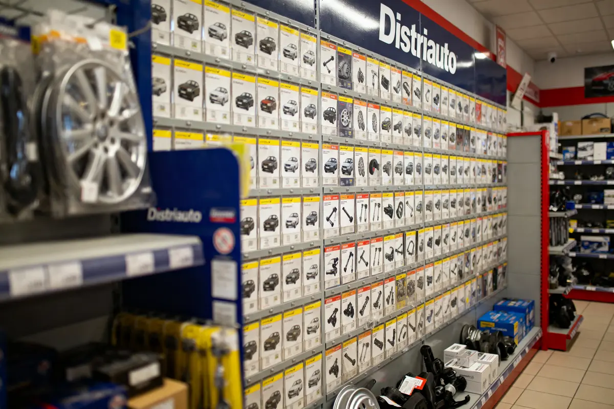 Mur d'affiches de pièces détachées automobiles dans un magasin, étagères à droite avec produits divers.