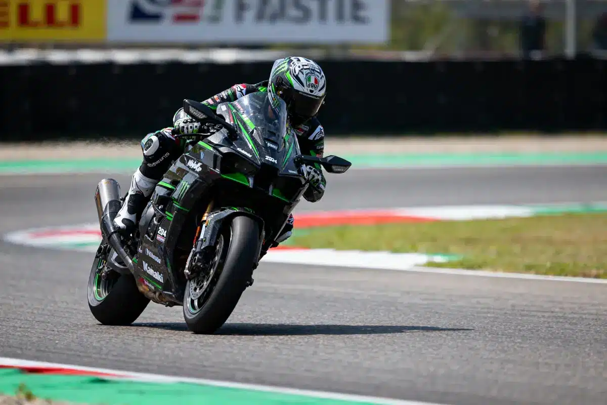 Motard en combinaison noire sur une Kawasaki verte, prenant un virage sur piste de course.