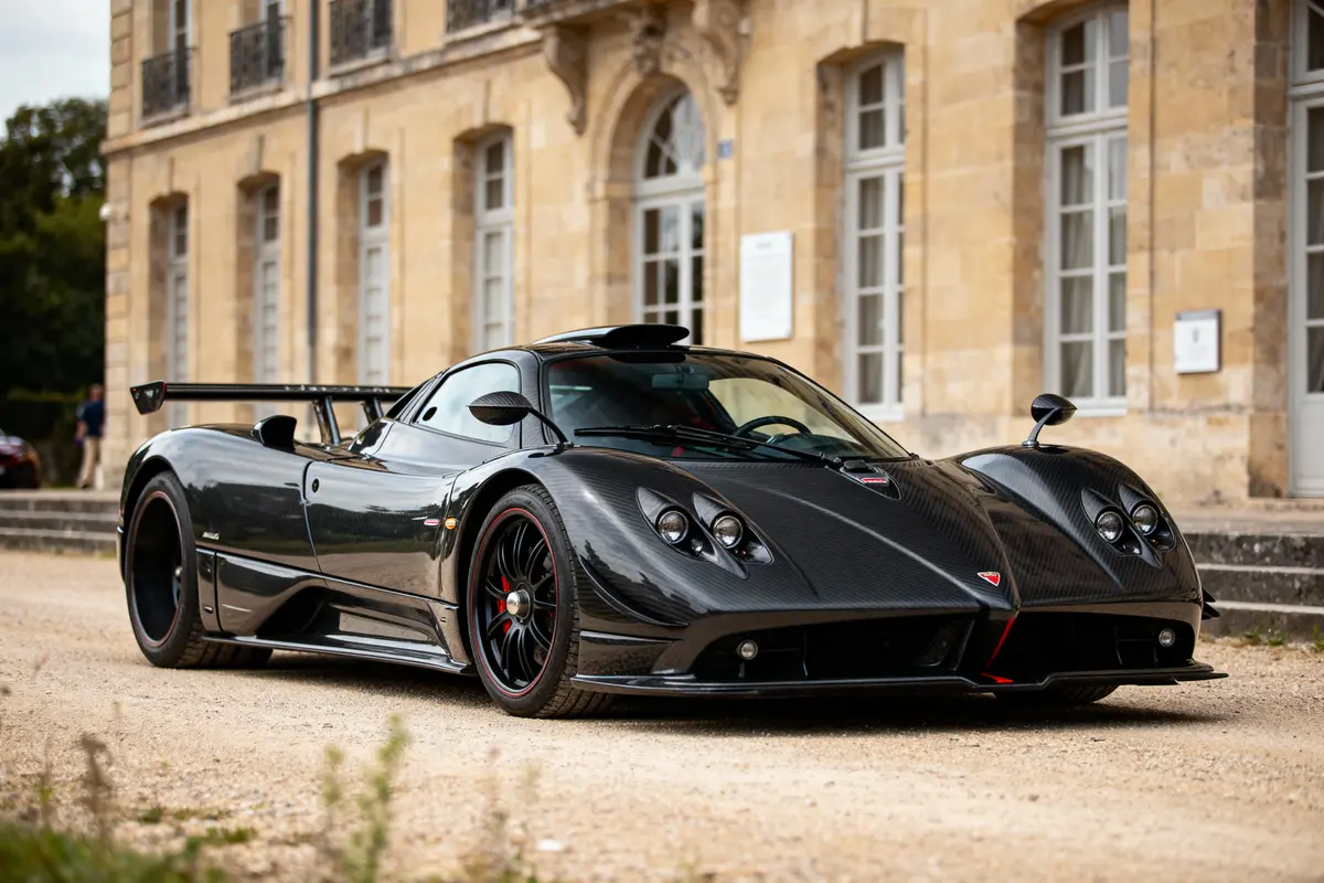 Voiture de sport noire garée devant un bâtiment historique en pierre, avec fenêtres à battants.