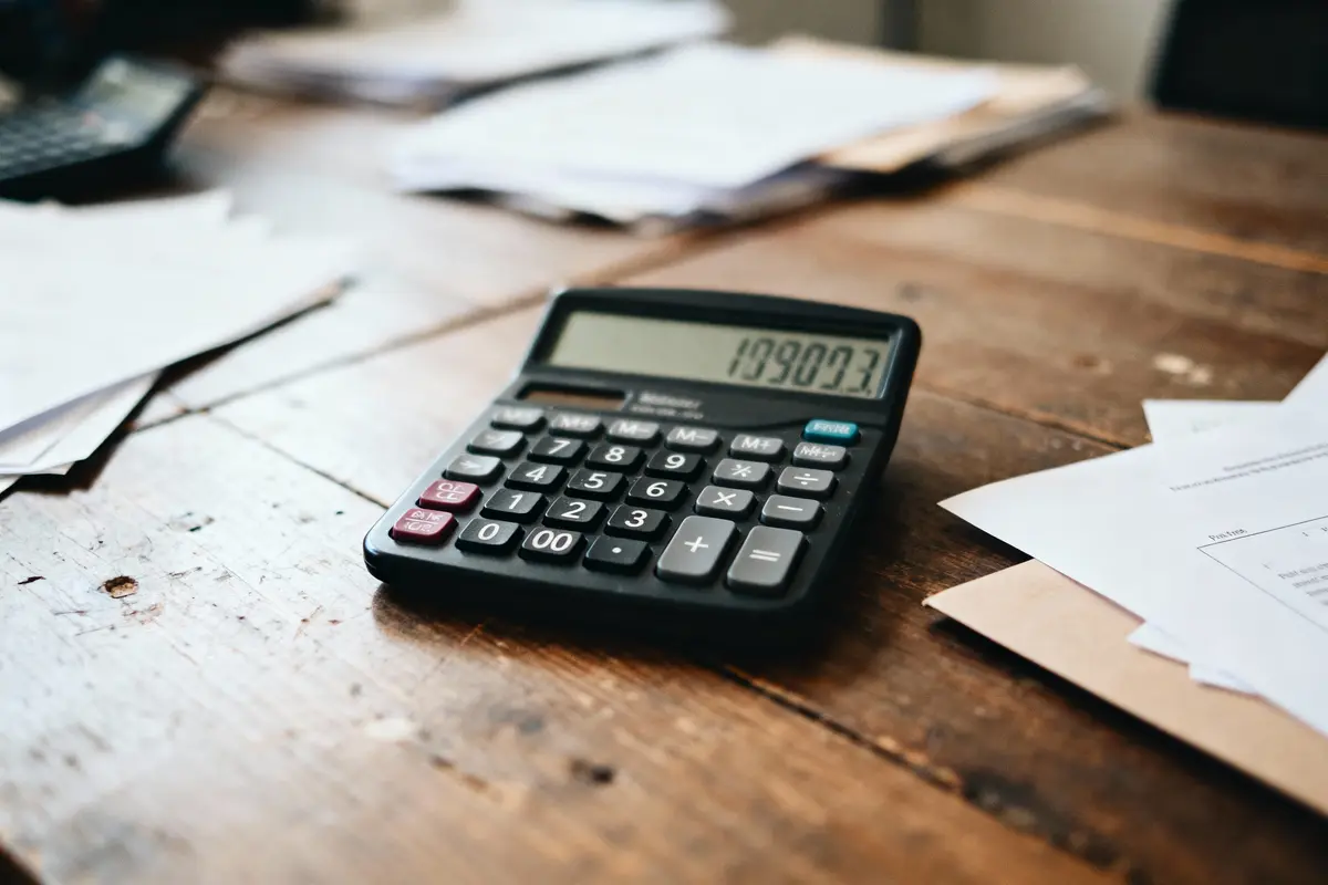 Calculatrice noire sur table en bois, entourée de documents et papiers, affichant 1090.73 sur l'écran.