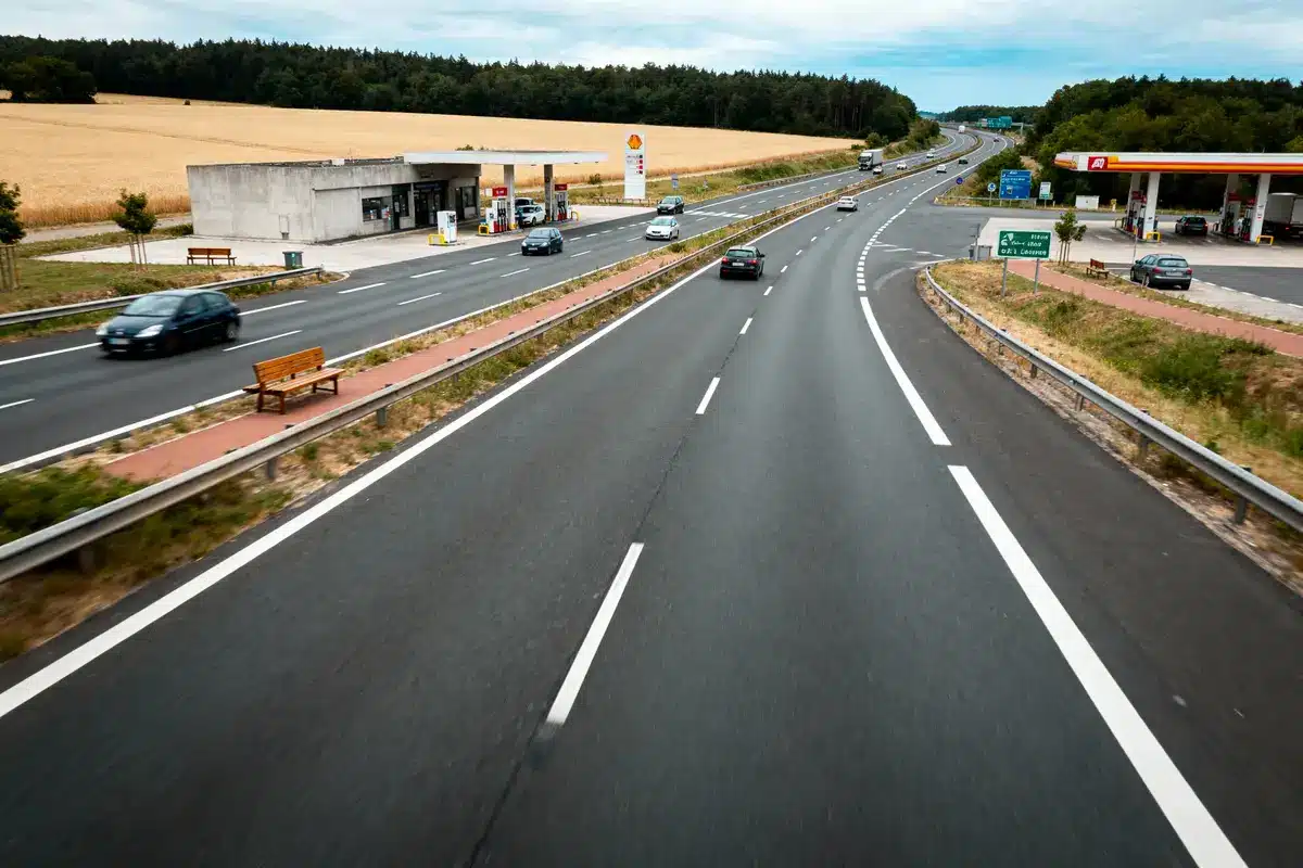 pexels-michal-pech-213601-757318 (1) Autoroute avec station-service Shell, voitures et paysages de campagne verdoyants sous ciel nuageux.