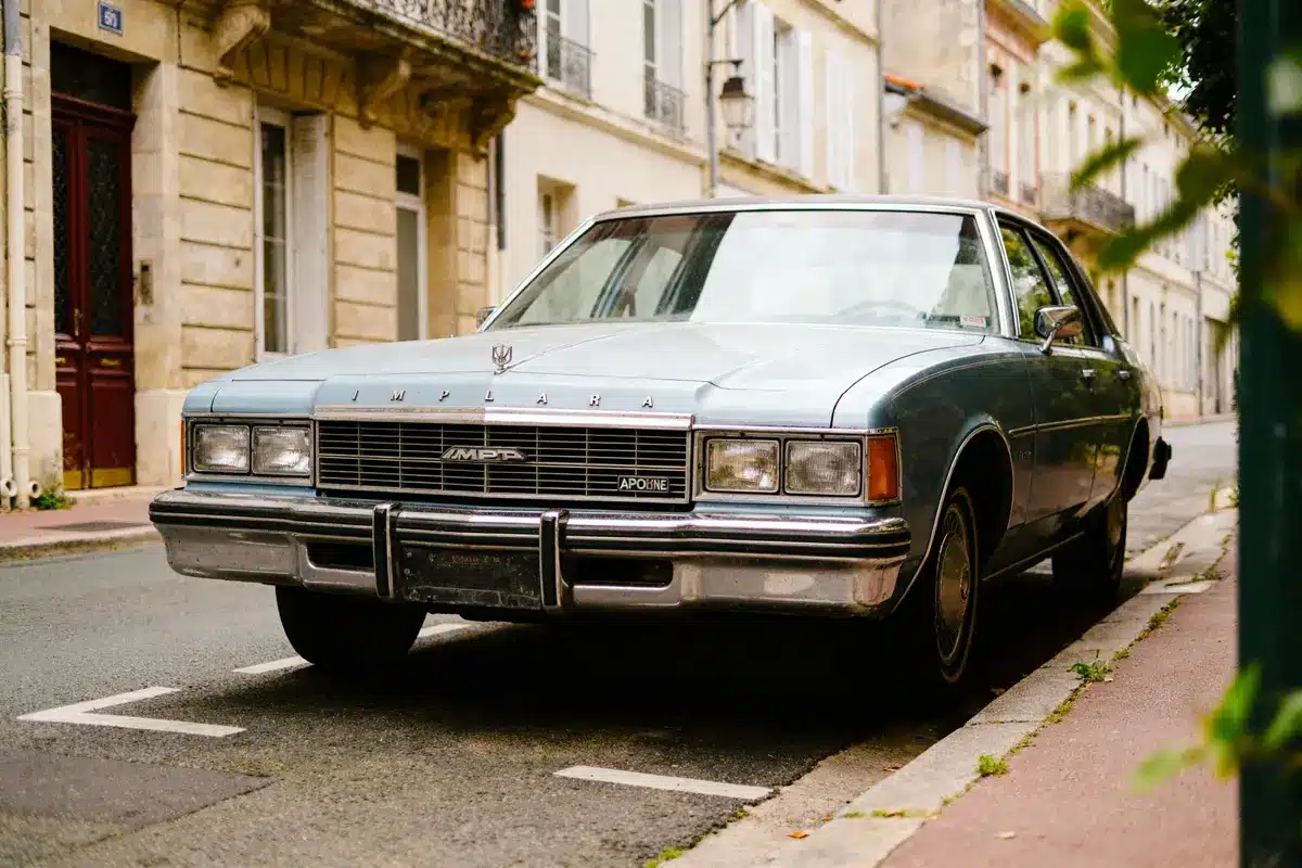 Voiture vintage bleue garée dans une rue pavée, devant des bâtiments anciens en pierre.