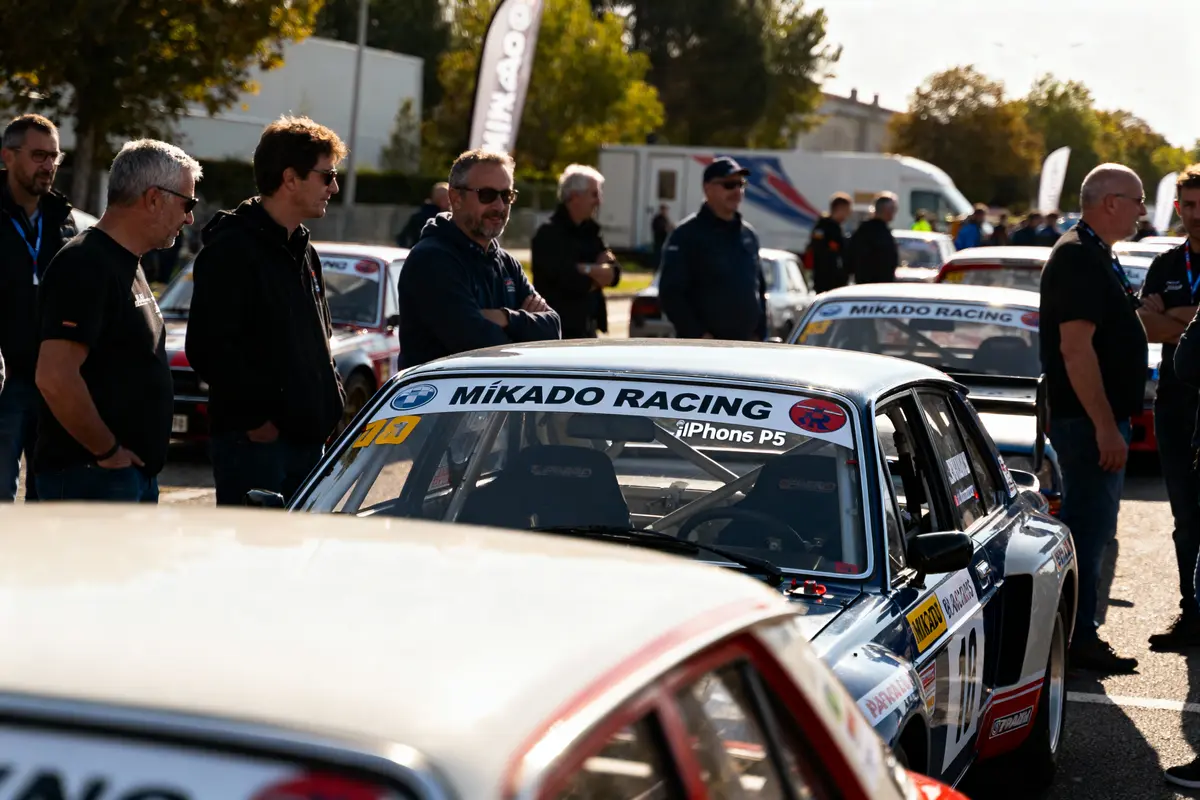 Groupe de personnes près de voitures de course Mikado Racing, en plein air, avec arbres en arrière-plan.