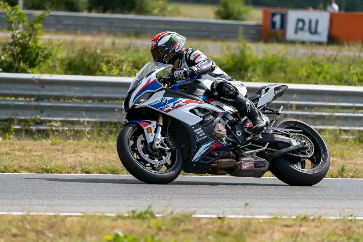 Motard en combinaison sur une moto BMW de course, prenant un virage sur un circuit en plein air.