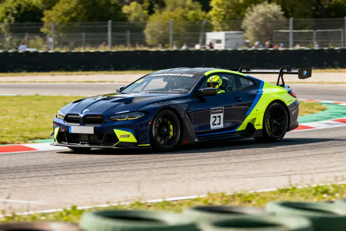 Voiture de course BMW bleue et verte sur circuit, numéro 27, tournant à grande vitesse.