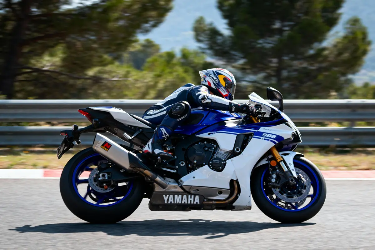 pexels-michal-pech-213601-757318 (1) Motard en combinaison sur une Yamaha bleue et blanche, roulant à vive allure sur circuit avec arbres en arrière-plan.