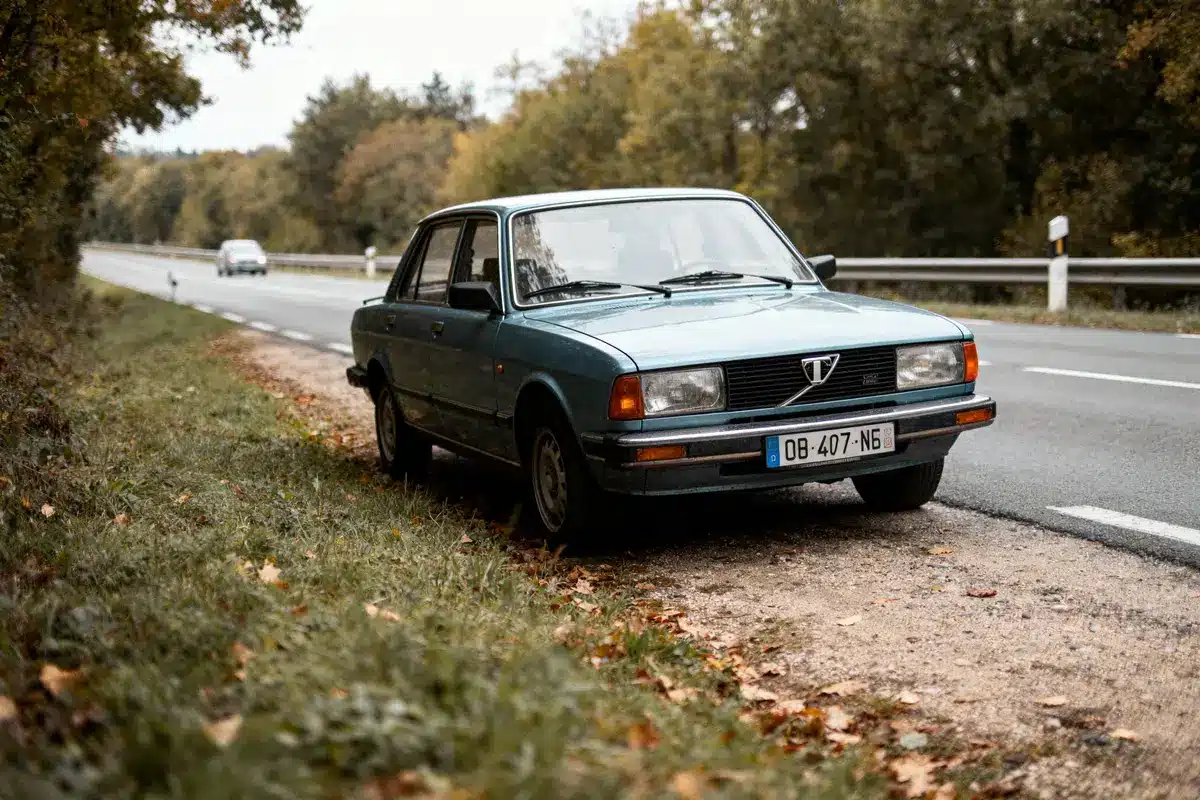 Voiture ancienne bleue garée au bord d'une route bordée d'arbres.