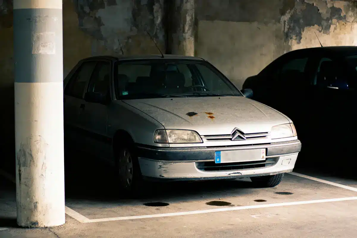 Voiture ancienne grise, garée dans un parking souterrain, avec traces de rouille sur le capot.