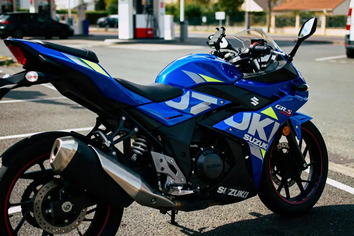 Moto Suzuki bleue garée à proximité d'une station-service, avec design sportif et lignes aérodynamiques.
