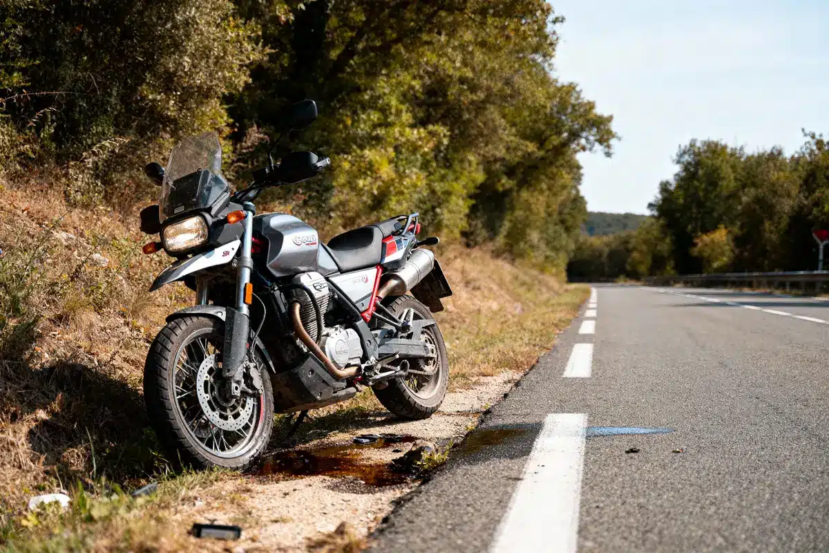 Moto stationnée sur le bord d'une route déserte, entourée d'arbres et de végétation.