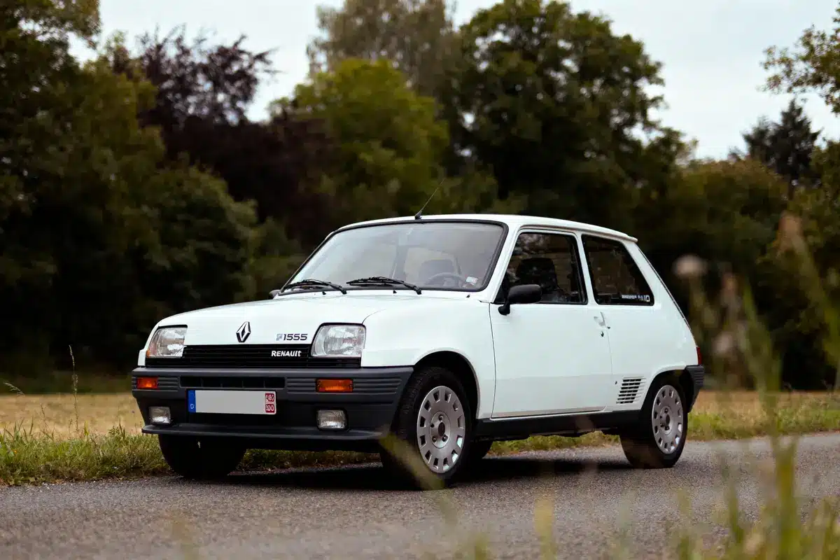 Voiture blanche Renault classique sur route devant des arbres. Éclairage naturel, ambiance rétro.
