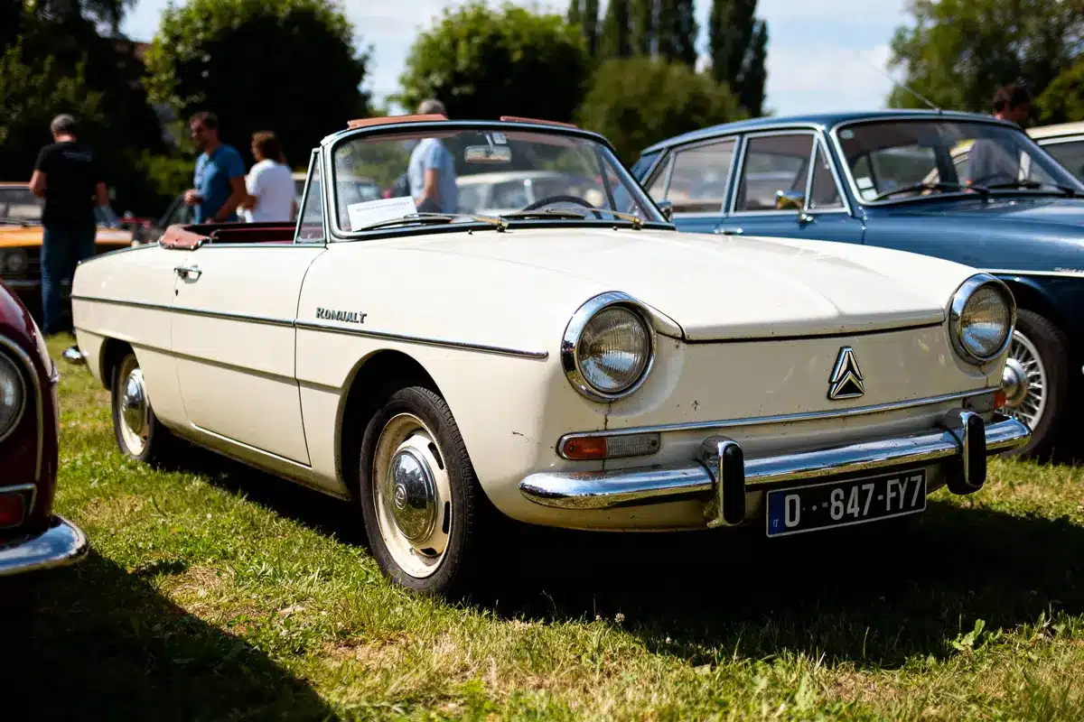 Voiture ancienne Renault Floride blanche lors d'une exposition en plein air, avec plusieurs personnes autour.