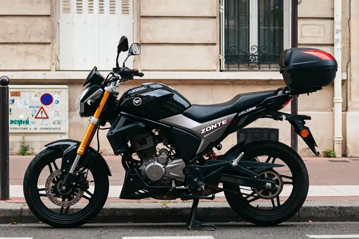 Moto noire Zontes stationnée sur la route devant un mur beige avec fenêtres.