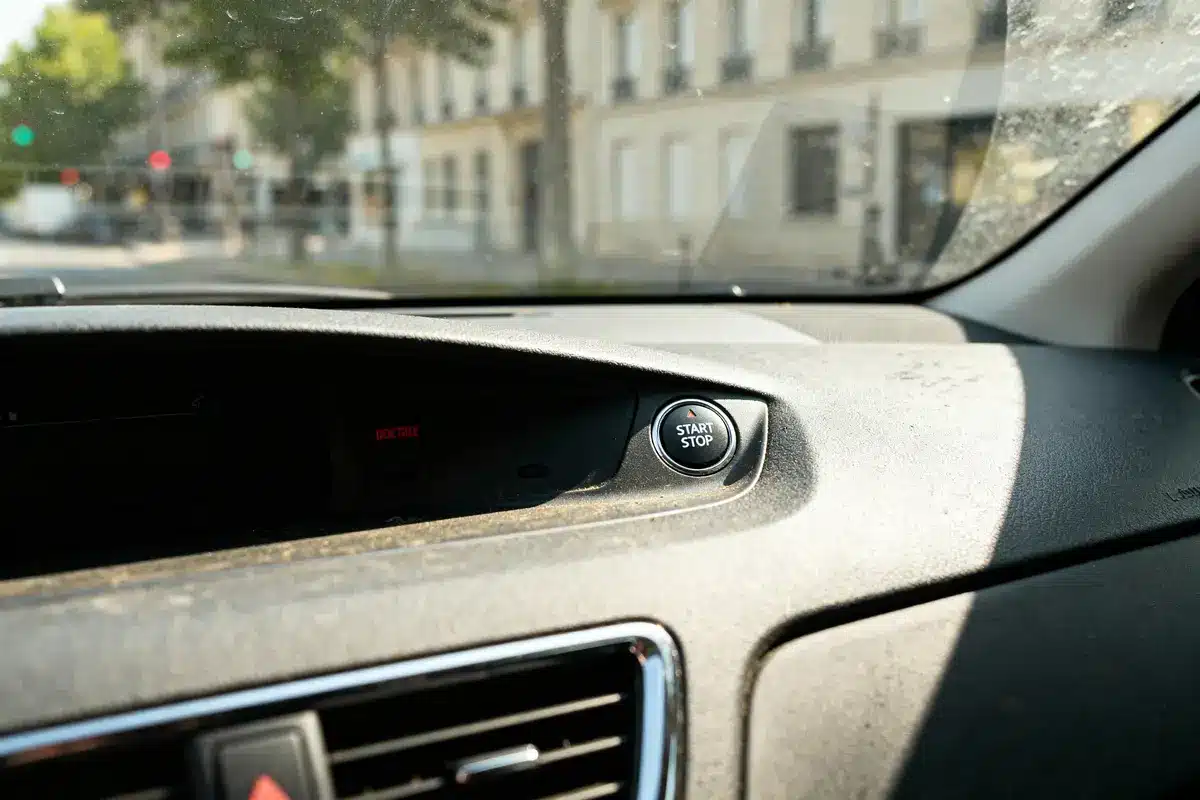 Bouton start-stop sur tableau de bord voiture, vue extérieure floue avec bâtiments et feu de signalisation.