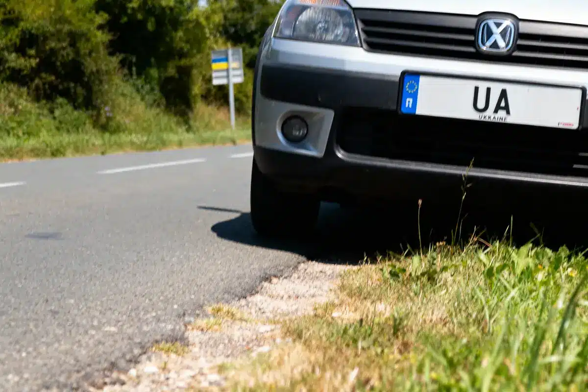 Gros plan d'une voiture sur le bas-côté d'une route, plaque ukrainienne visible, panneaux flous.