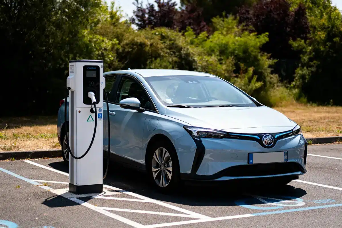 Voiture électrique argentée en charge à une borne, stationnement réservé, avec arrière-plan verdoyant.