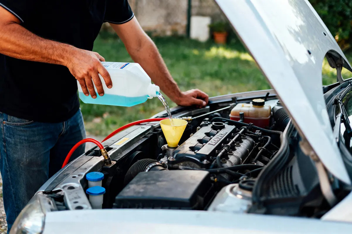pexels-michal-pech-213601-757318 (1) Personne versant liquide de refroidissement sous le capot ouvert d'une voiture avec un entonnoir jaune.
