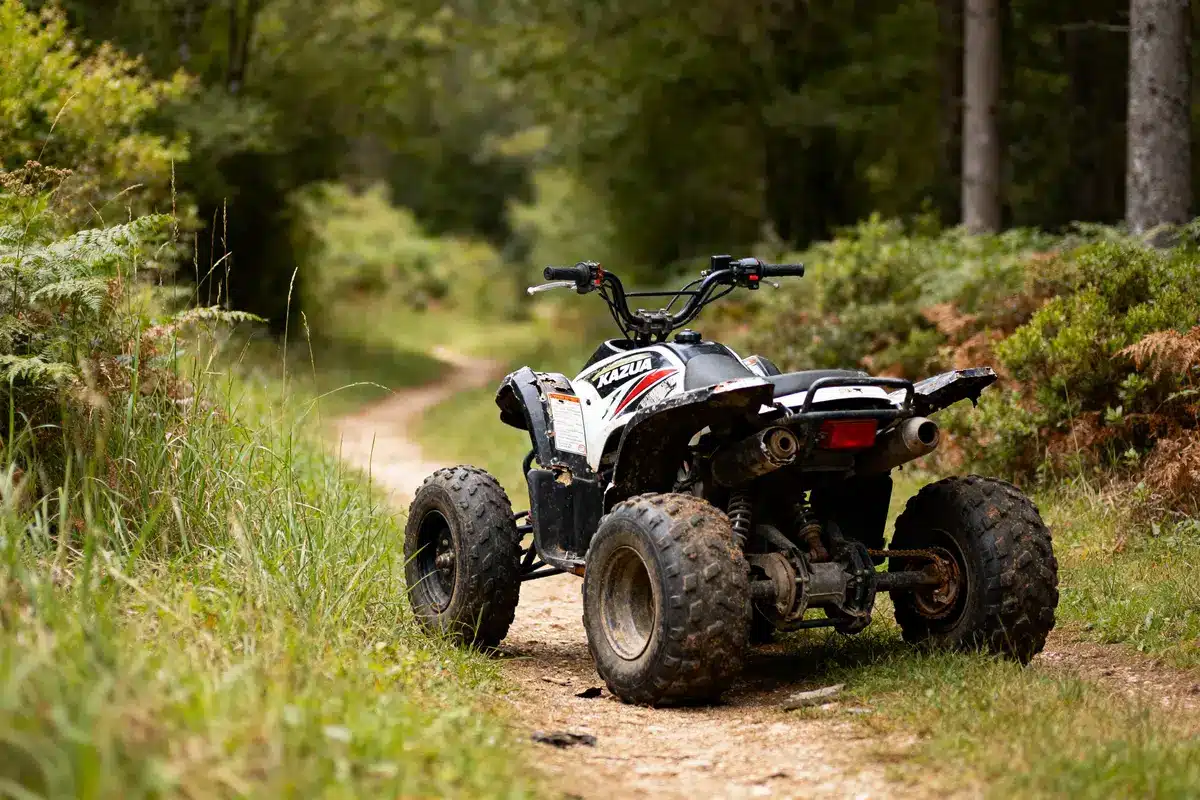 Quad stationné sur un chemin de terre entouré de verdure et de forêt.