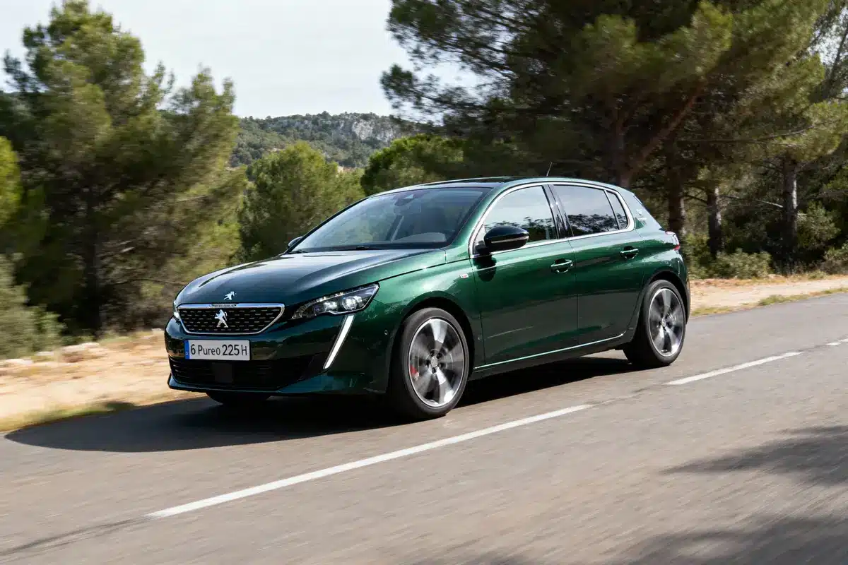 Voiture verte, cinq portes, roulant sur route bordée d'arbres et de collines, ciel clair.