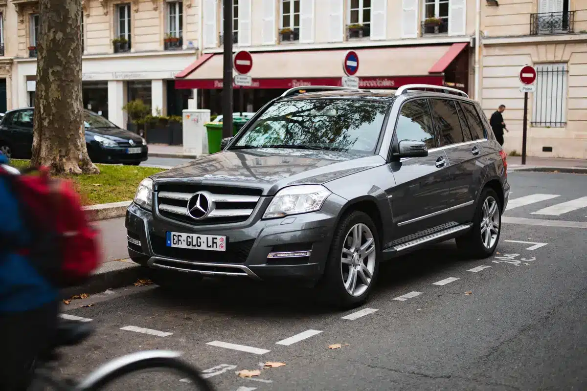 SUV gris Mercedes stationné dans une rue urbaine avec cycliste flou au premier plan.