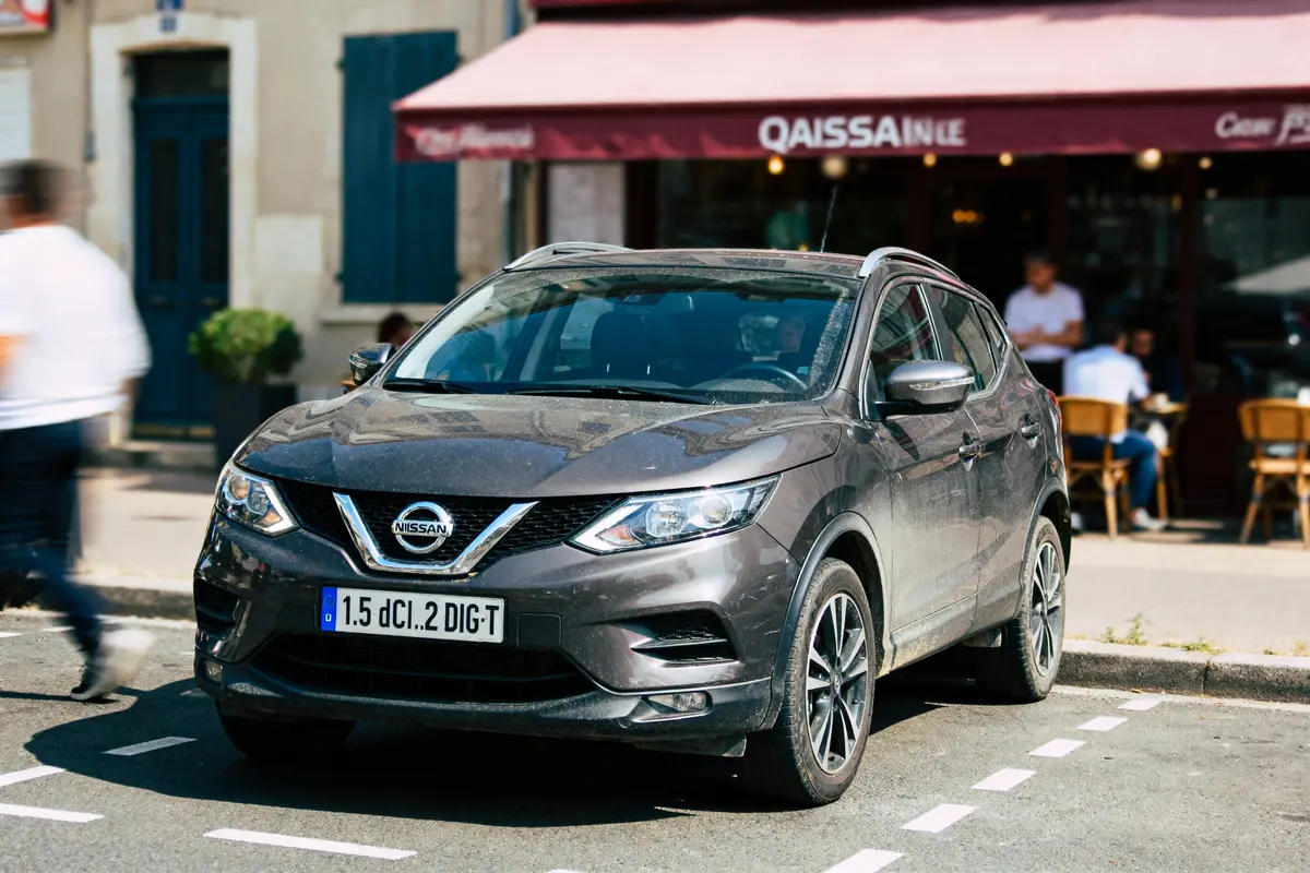 pexels-michal-pech-213601-757318 (1) Voiture Nissan grise garée devant un café, personnes assises en terrasse, rue animée.