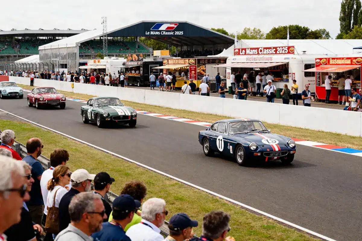 Courses de voitures classiques au Mans Classic 2025 avec stand alimentaire, spectateurs et voitures anciennes sur piste.
