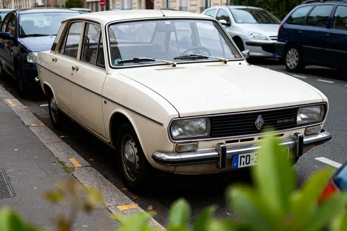 Voiture vintage Renault beige, garée en parallèle sur une rue urbaine. Autres voitures visibles en arrière-plan.