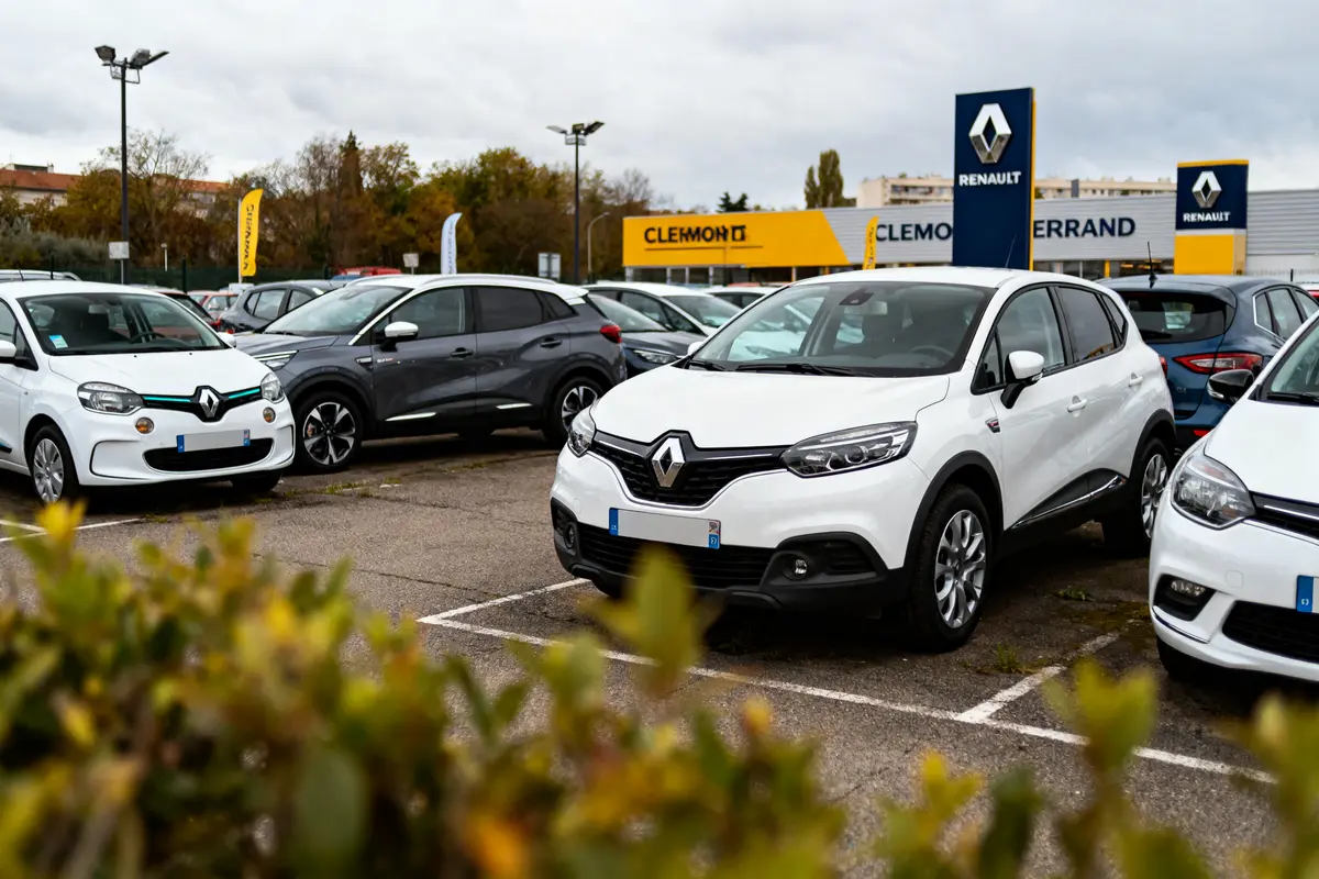 Voitures blanches Renault stationnées devant concession Renault, enseignes visibles, ciel nuageux.