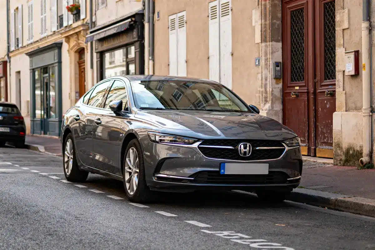 pexels-michal-pech-213601-757318 (1) Voiture grise Honda stationnée dans une rue pavée, bordée de bâtiments anciens et boutiques.