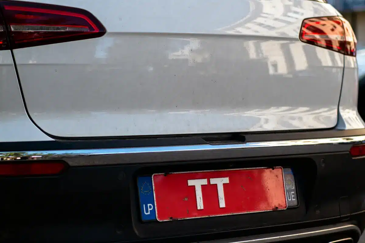 Plaque d'immatriculation rouge "TT" sur une voiture blanche avec feux arrière visibles.