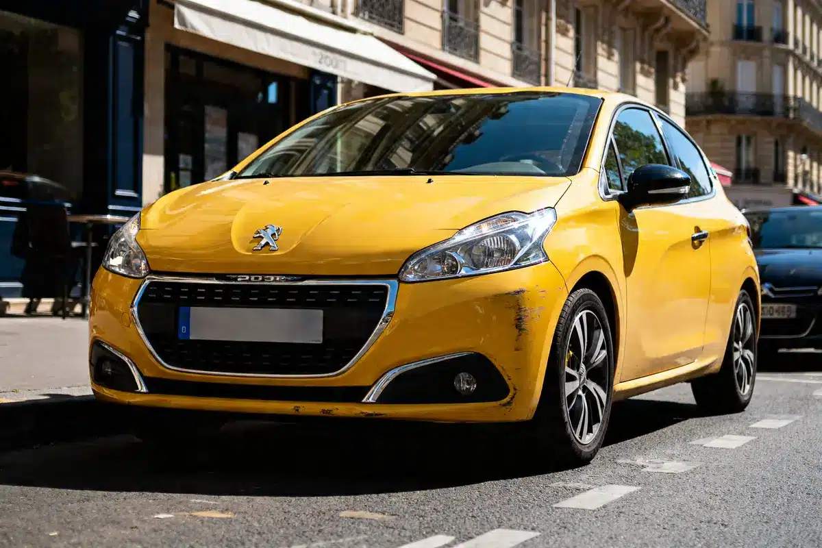 Voiture 208 jaune garée en ville, avec éraflures visibles sur le pare-choc avant