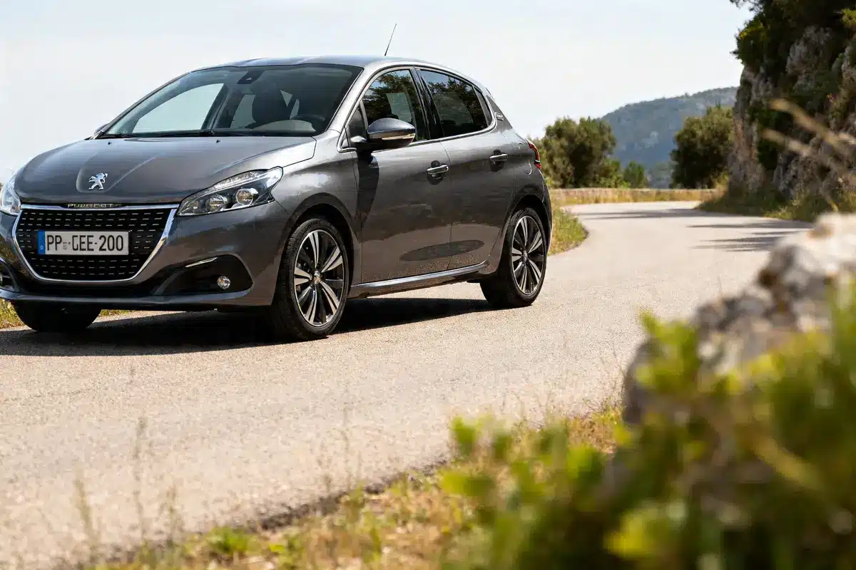Peugeot 208 gris roulant sur une route sinueuse bordée de végétation luxuriante