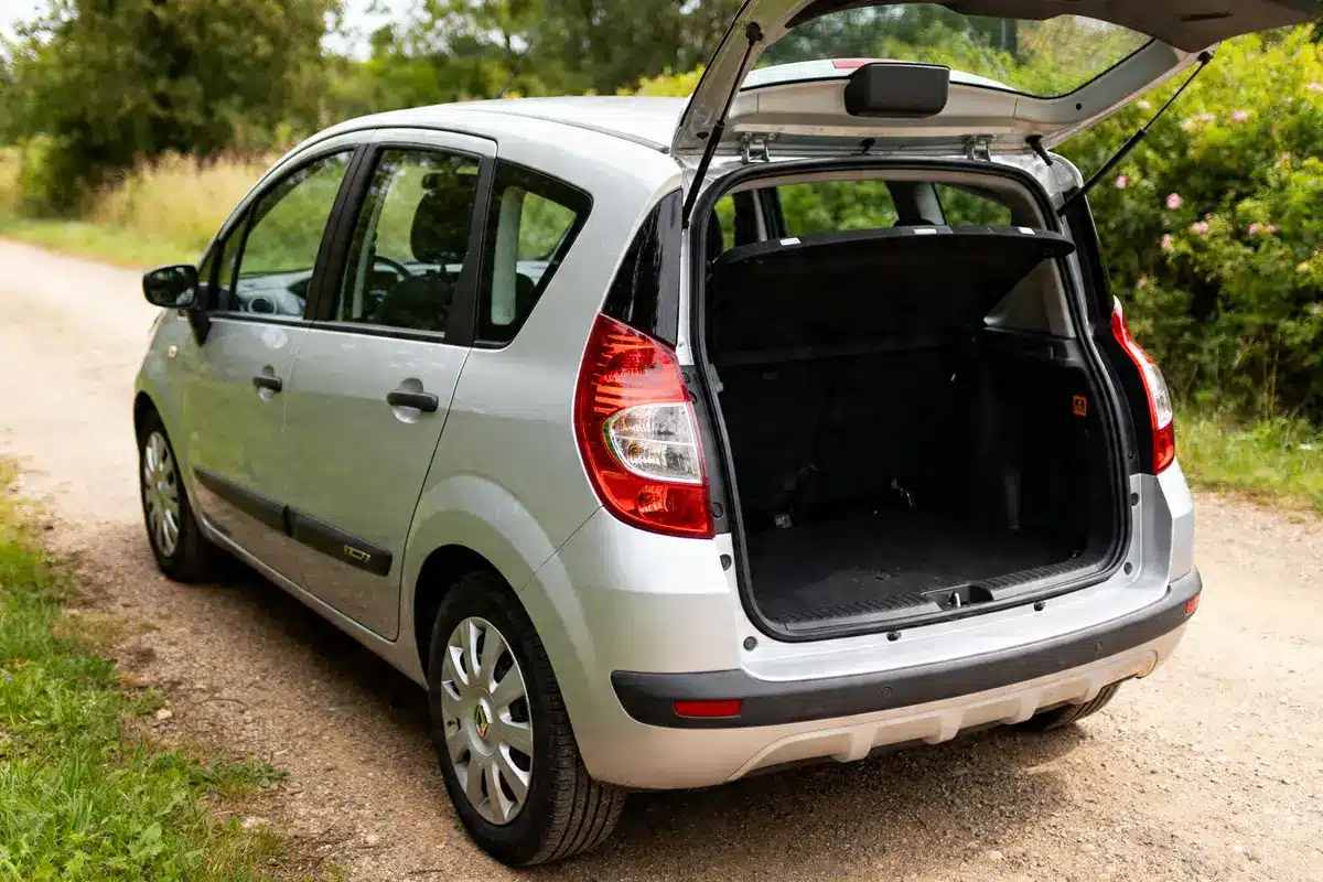 Renault Modus argentée stationnée avec coffre ouvert sur chemin de campagne.
