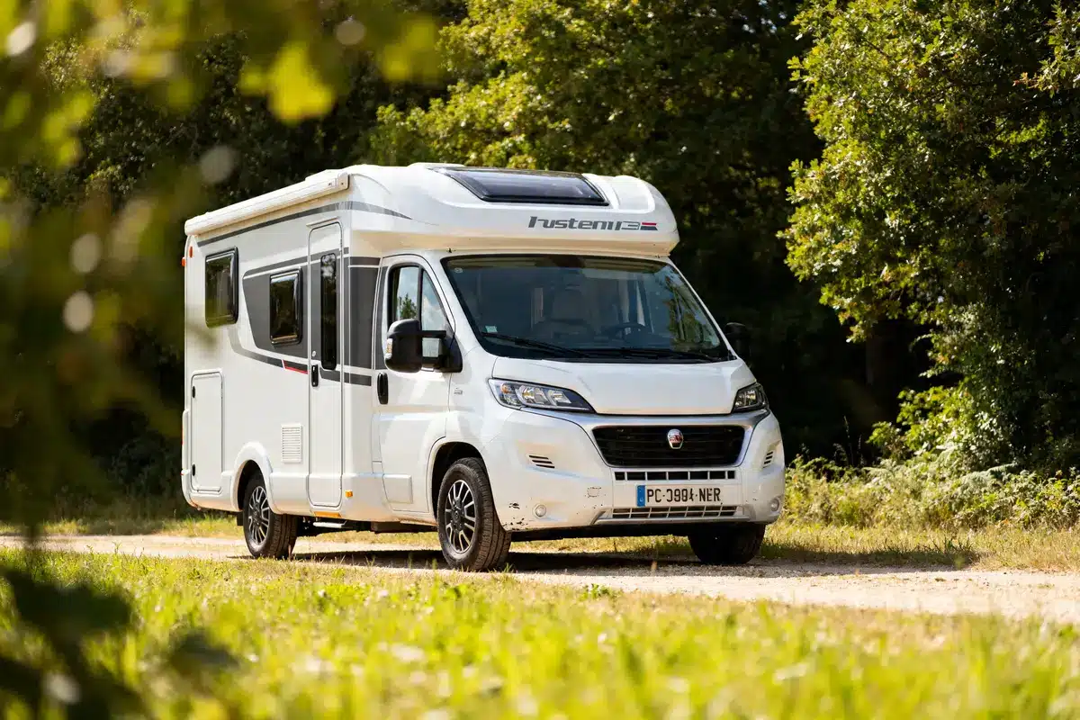 Camping-car neuf pas cher blanc garé dans un chemin entouré d'arbres verdoyants