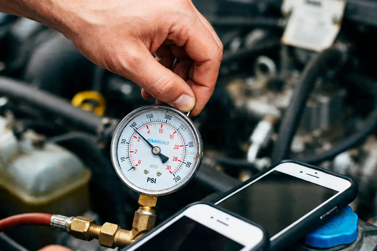 Main qui tient un manomètre pour change psi to bar dans un moteur de voiture