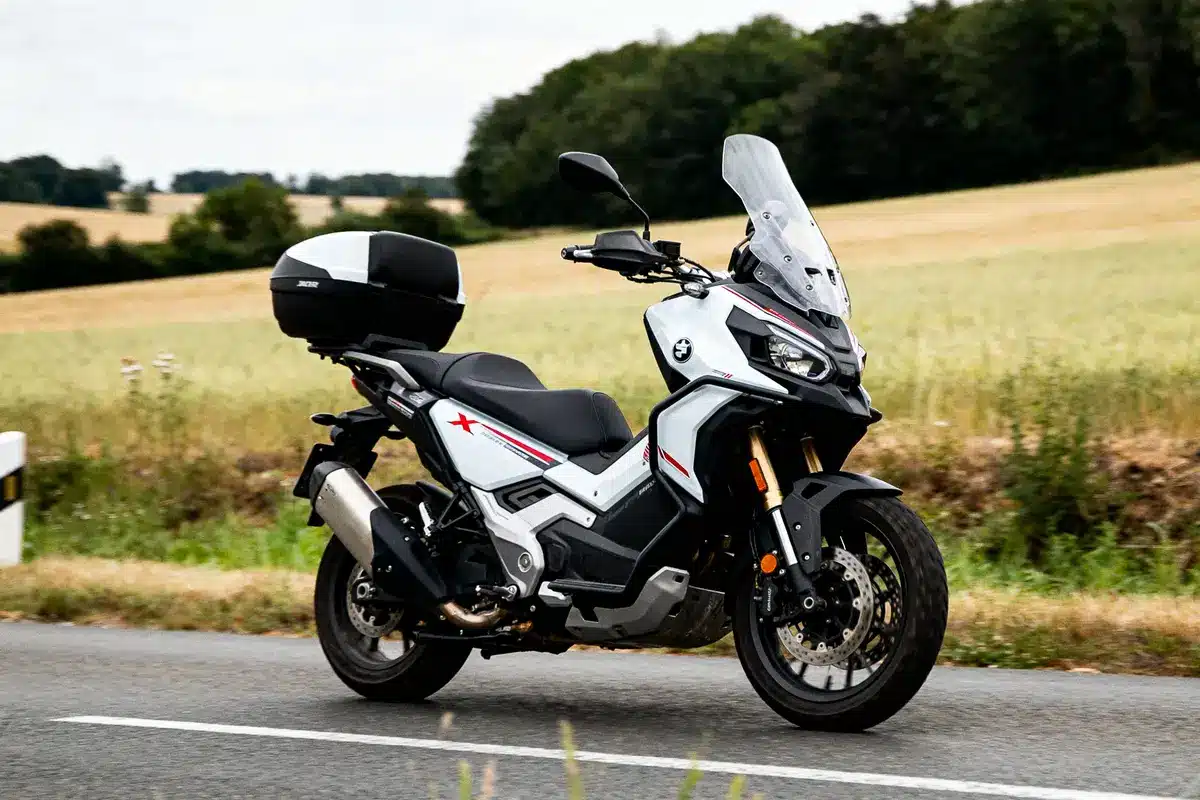 Moto X ADV blanche roulant sur route de campagne avec paysage rural en arrière-plan
